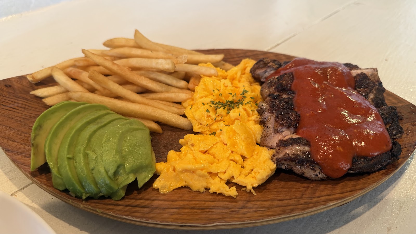 Grilled chicken plate with scrambled eggs, fries, and sliced avocado